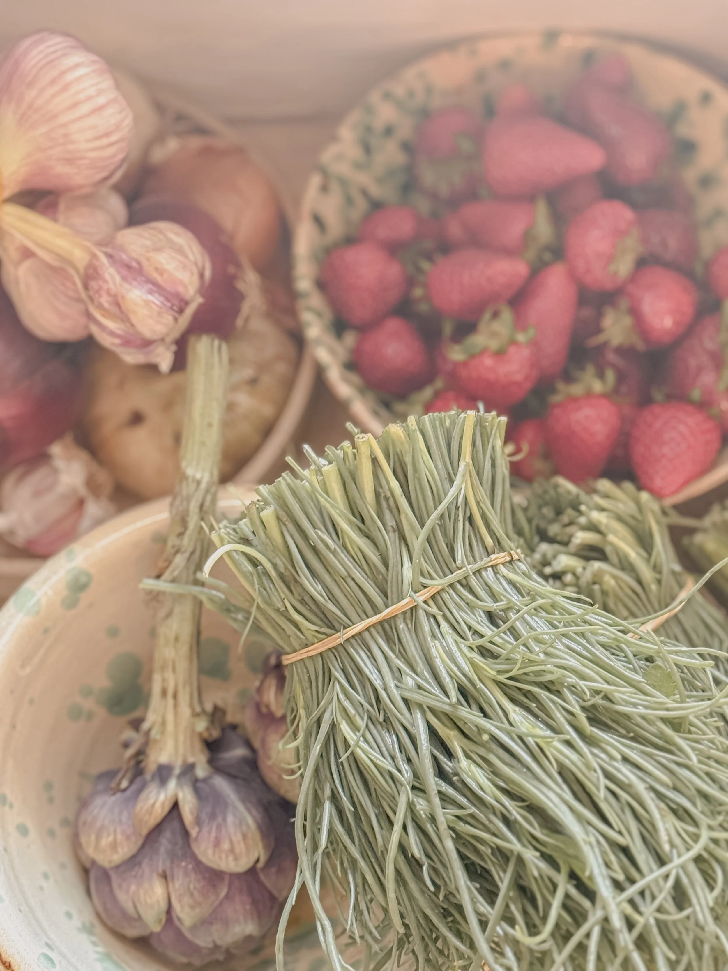Fresh garlic, strawberries, and a bunch of dried rosemary in bowls.