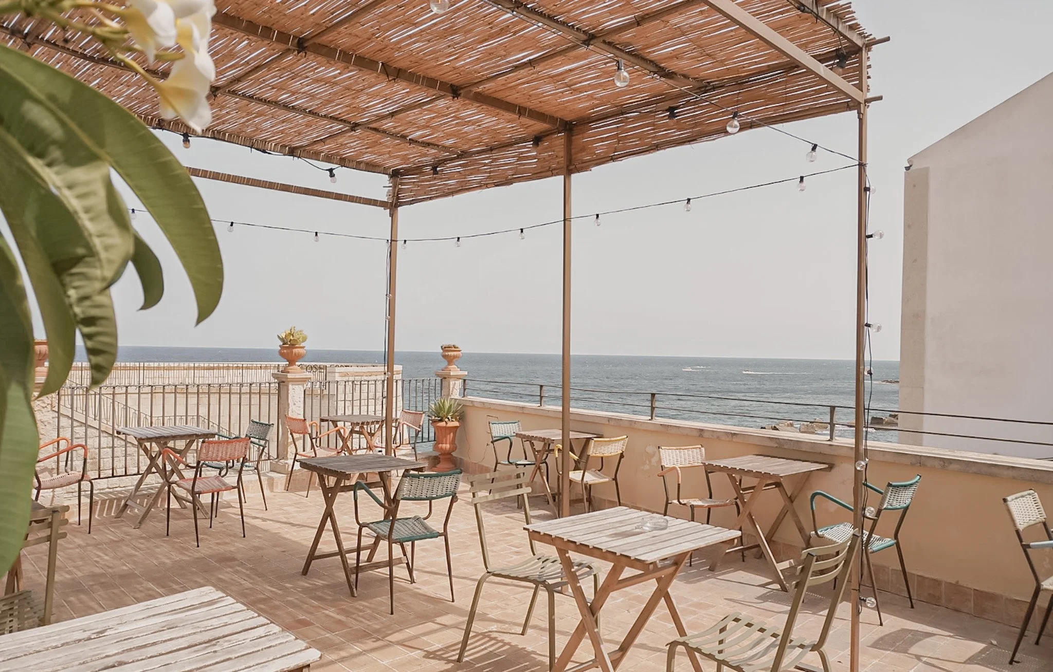Outdoor terrace with seating, tables, and string lights overlooking the ocean.