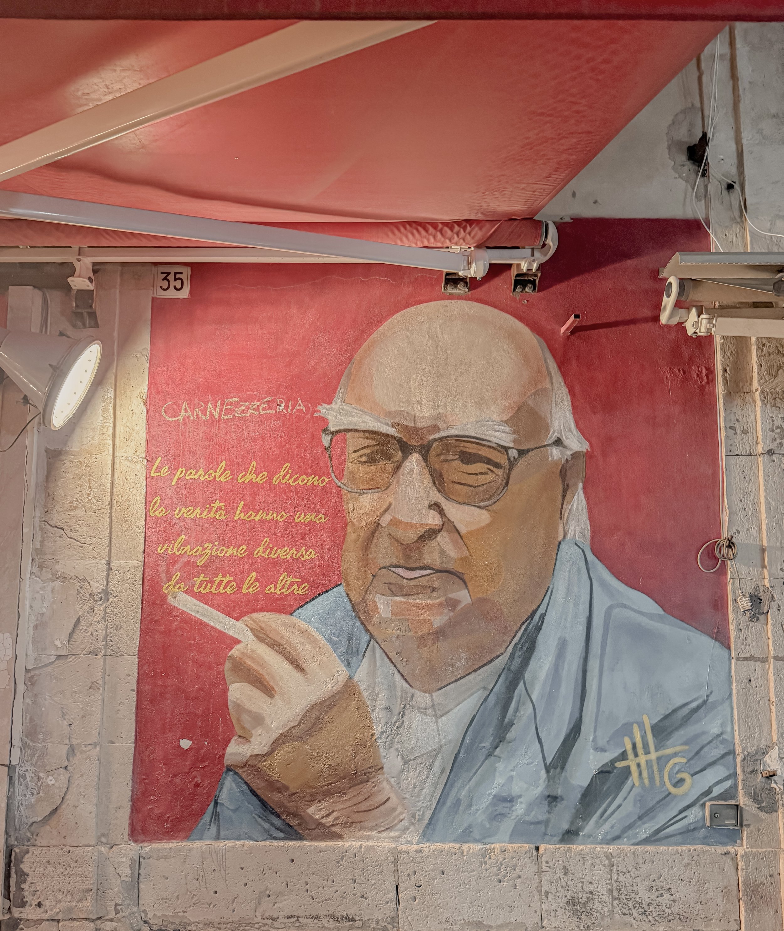 Murals of an elderly man with glasses, holding a cigarette, with Italian text on a red background.
