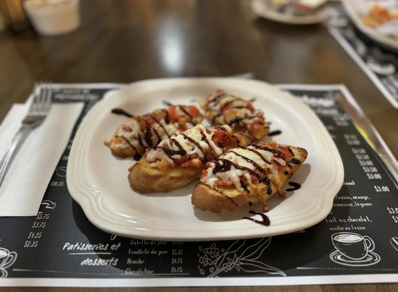 Bruschetta garnie de fromage, légumes, et sauce chocolat, servie sur une assiette blanche.
