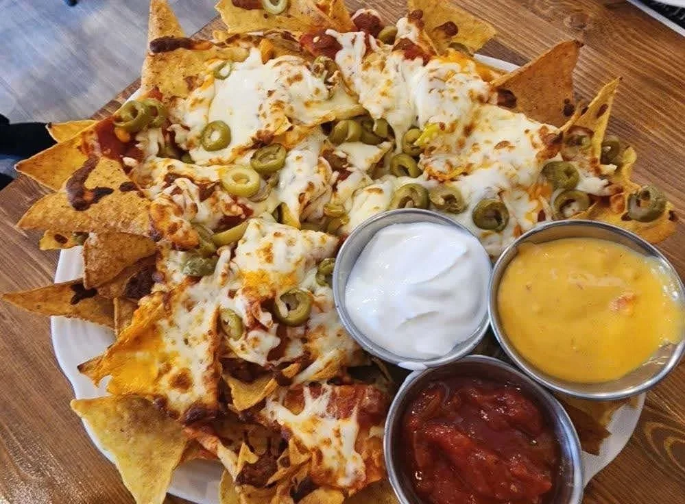 Un plateau de nachos garnis de fromage fondu, jalapeños, et accompagnés de trois sauces : crème, fromage et salsa.