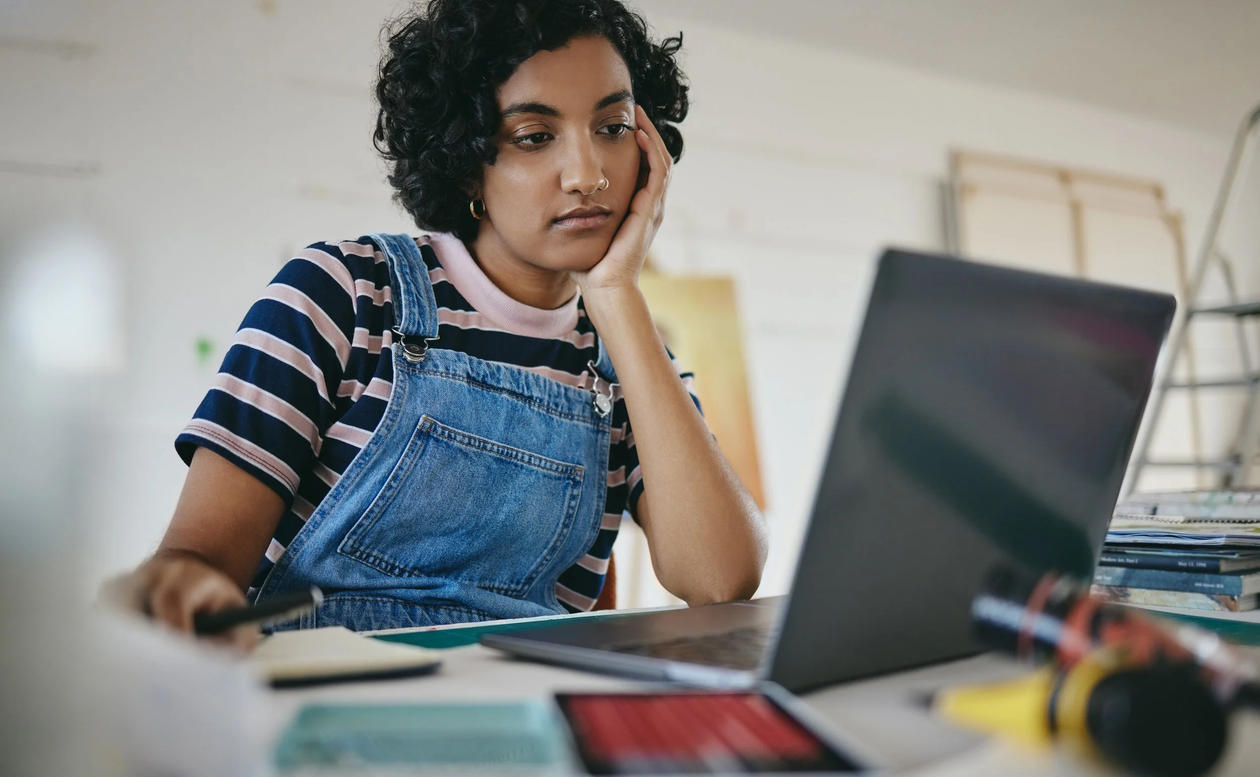 A distracted young woman stares at a laptop but do not look like she is focusing on the work she is doing