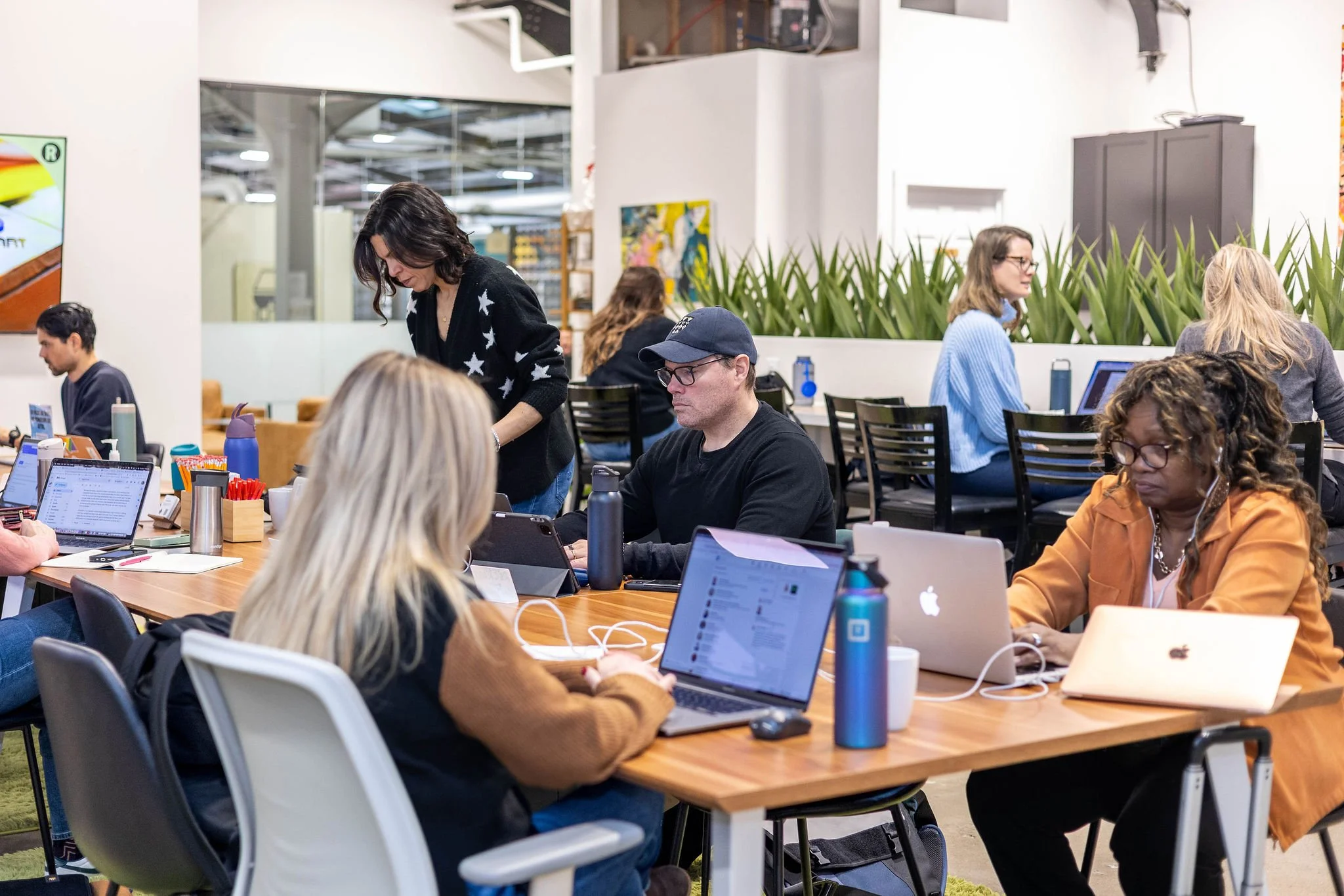 People working on laptops at a shared office space in a modern, open environment with plants and artwork.