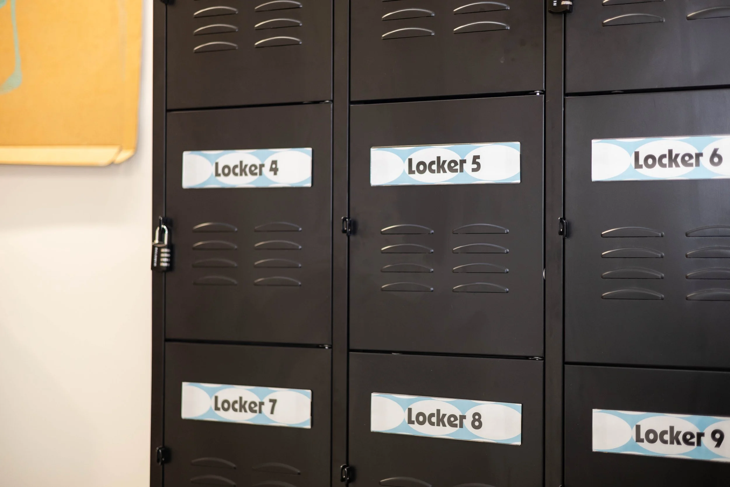 A row of black metal lockers labeled Locker 4 through Locker 9, with part of a yellow bulletin board visible on the left.
