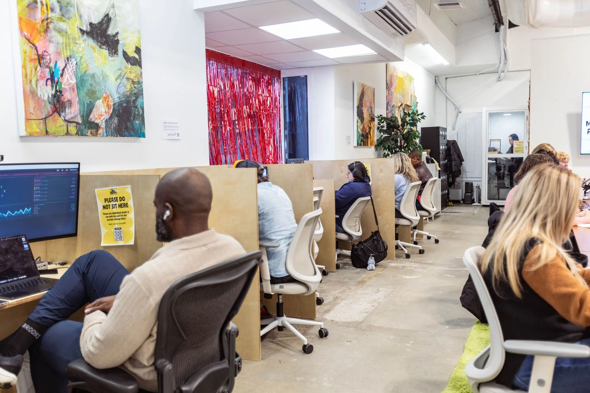People working at desks in an office with abstract artwork on the walls and a red curtain in the background.