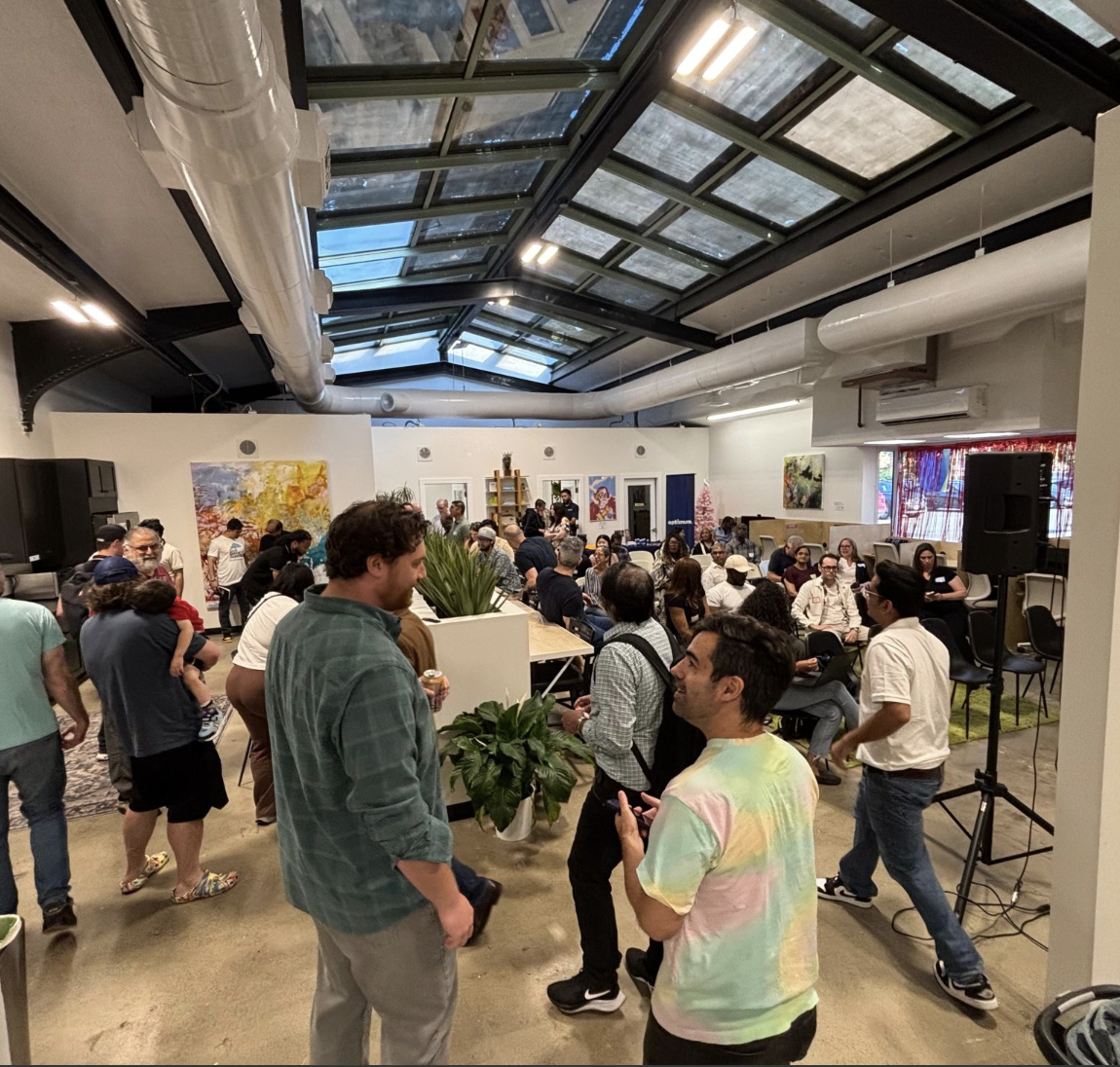 People socializing and mingling in a spacious, modern indoor venue with artwork on the walls and a skylight ceiling.