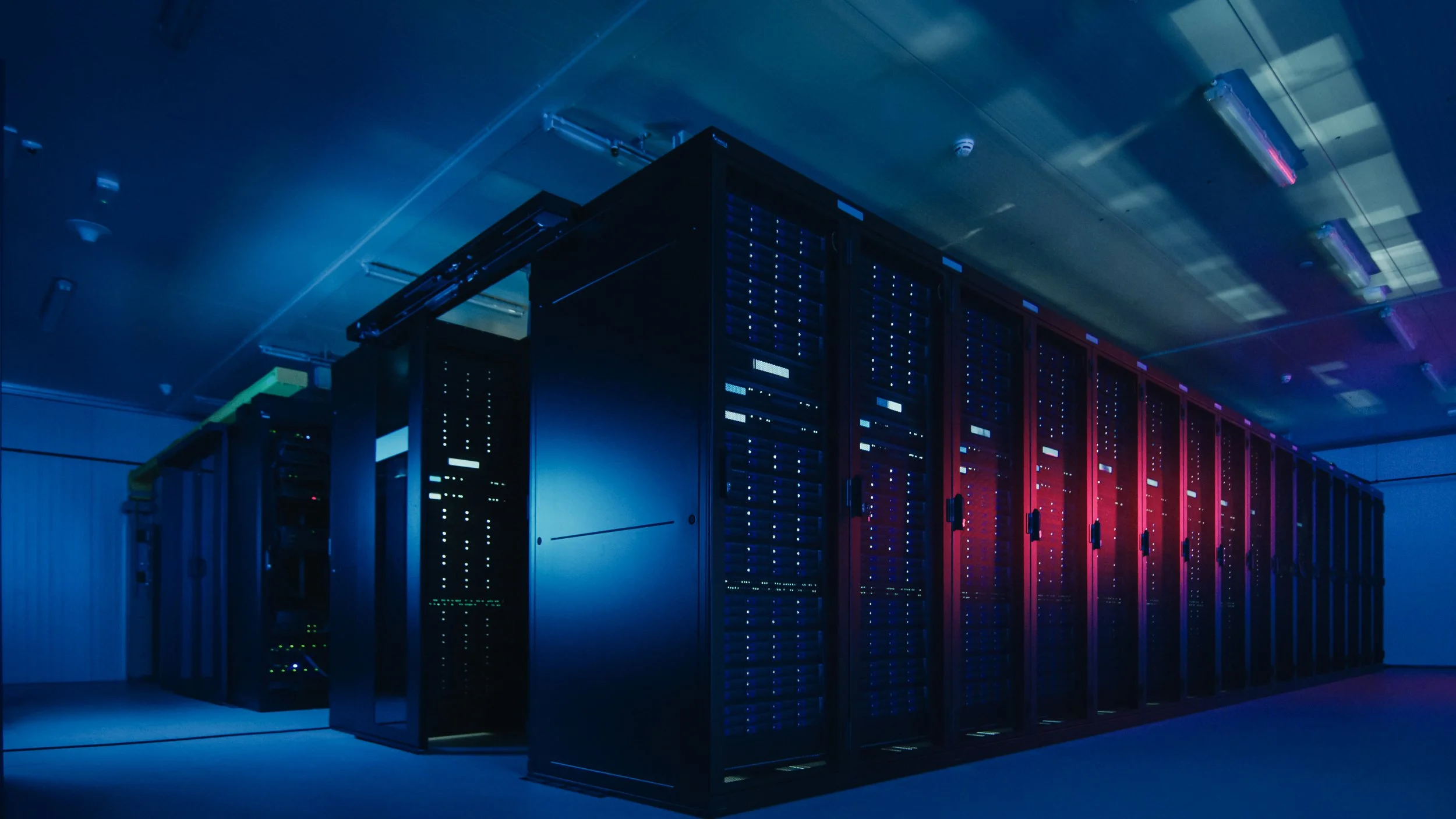 A server room with multiple black server racks lit by blue and red LED lights. Whether you're testing white space or external chiller plants, our equipment ensures accuracy and reliability.
