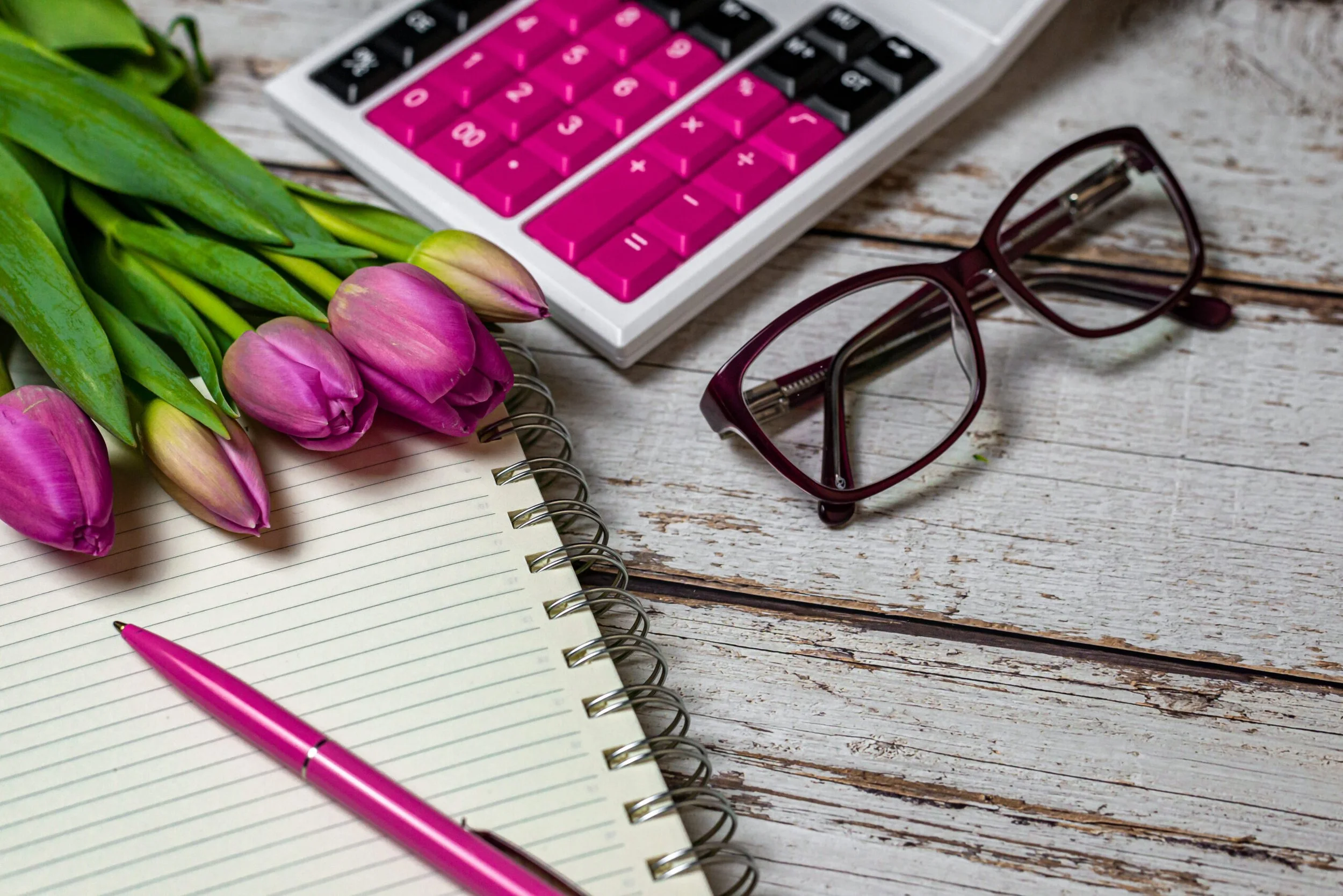 A spring lay flat image with tulips, a calculator, a notebook, a pen, and glasses.