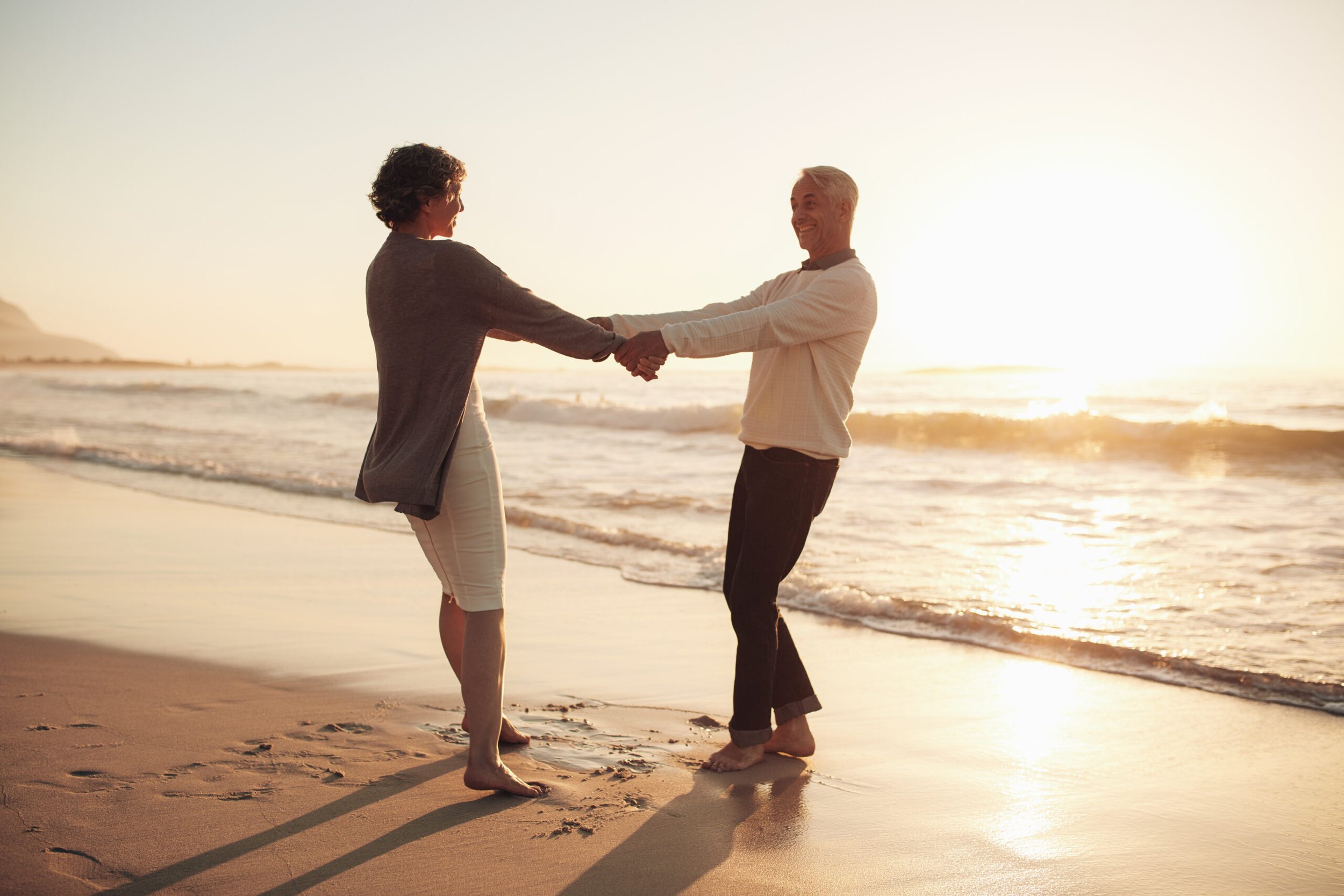 A couple spinning in a circle on the beach while holding hands.