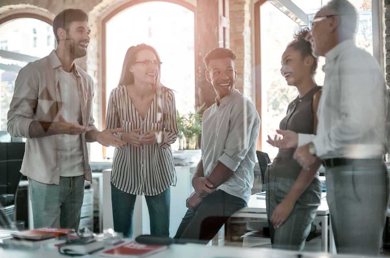 A team of employees standing around a desk laughing and smiling.