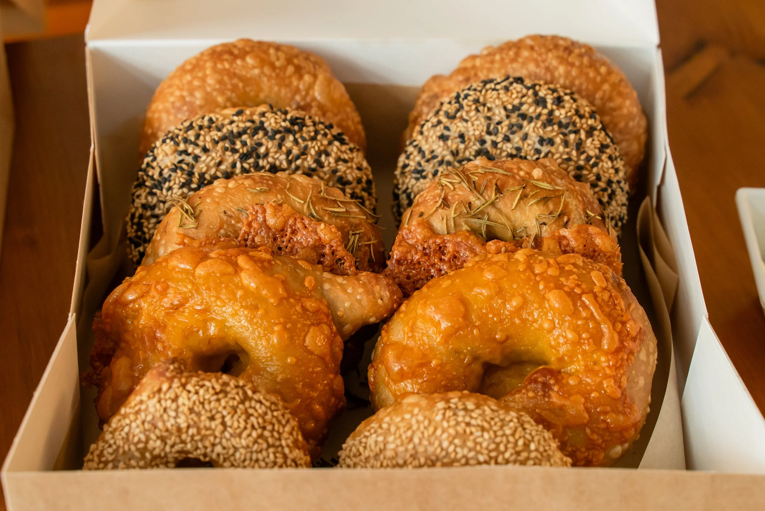 A box of assorted donuts including glazed, sesame seed, and seedless varieties.