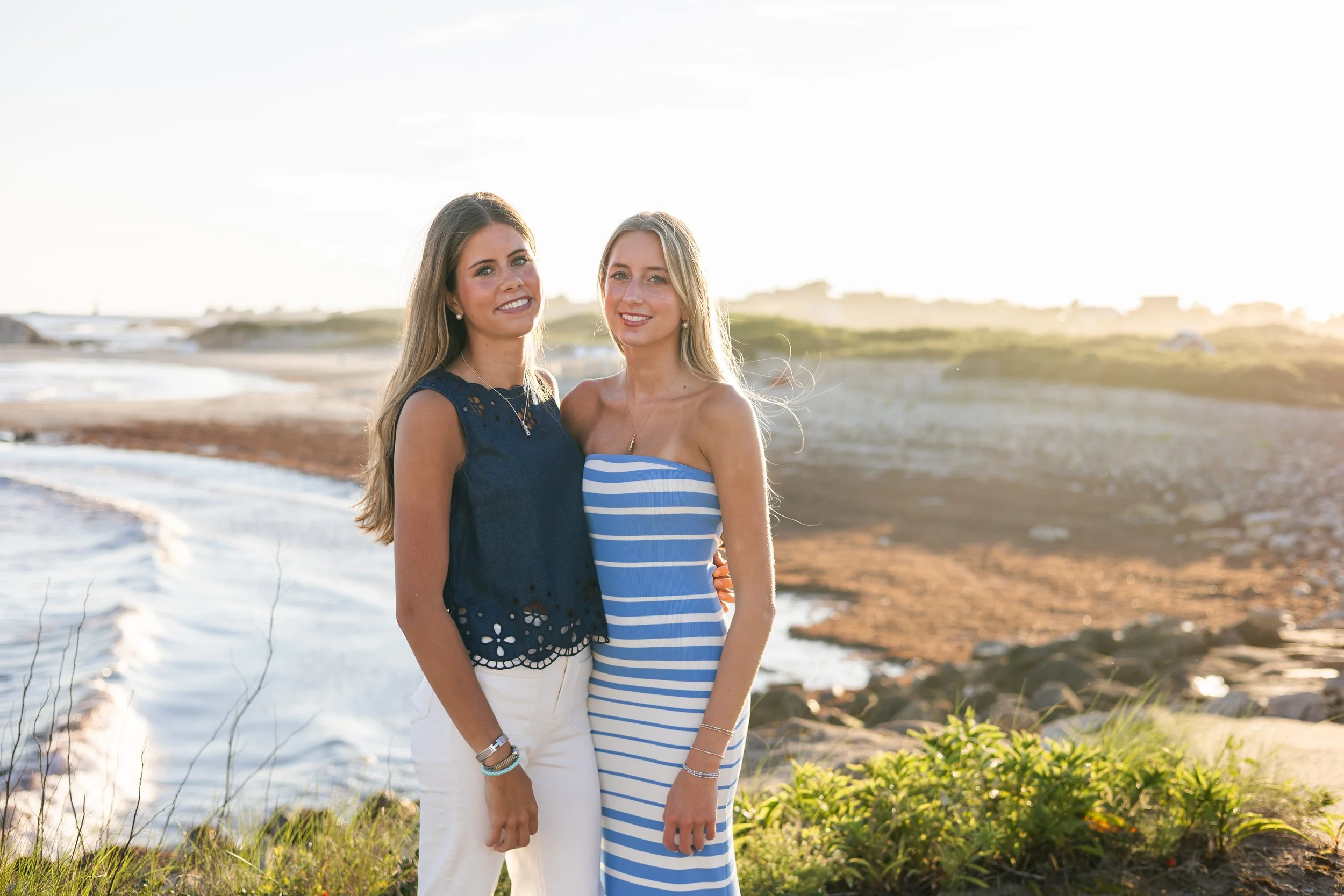 Two women standing on a beach with the ocean and sandy shoreline in the background, during sunset or sunrise.