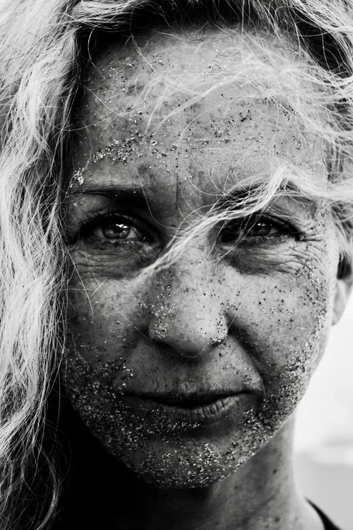 Close-up black and white photo of a woman with sand on her face and flowing hair.