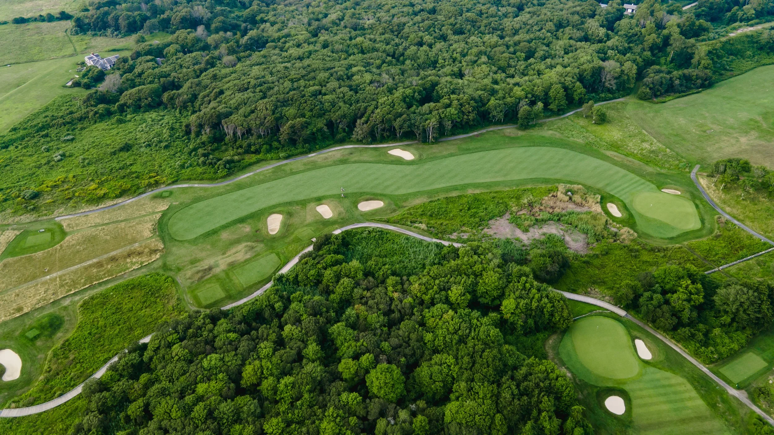 An aerial view of a golf course with green fairways, sand bunkers, and trees surrounding the course.