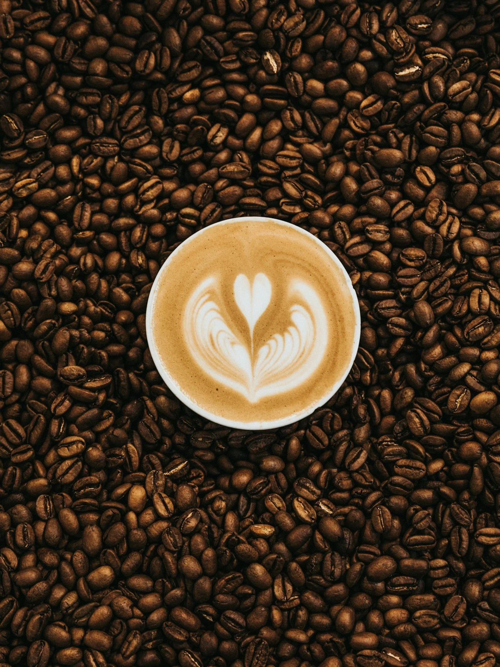 A cup of coffee with latte art, surrounded by roasted coffee beans.