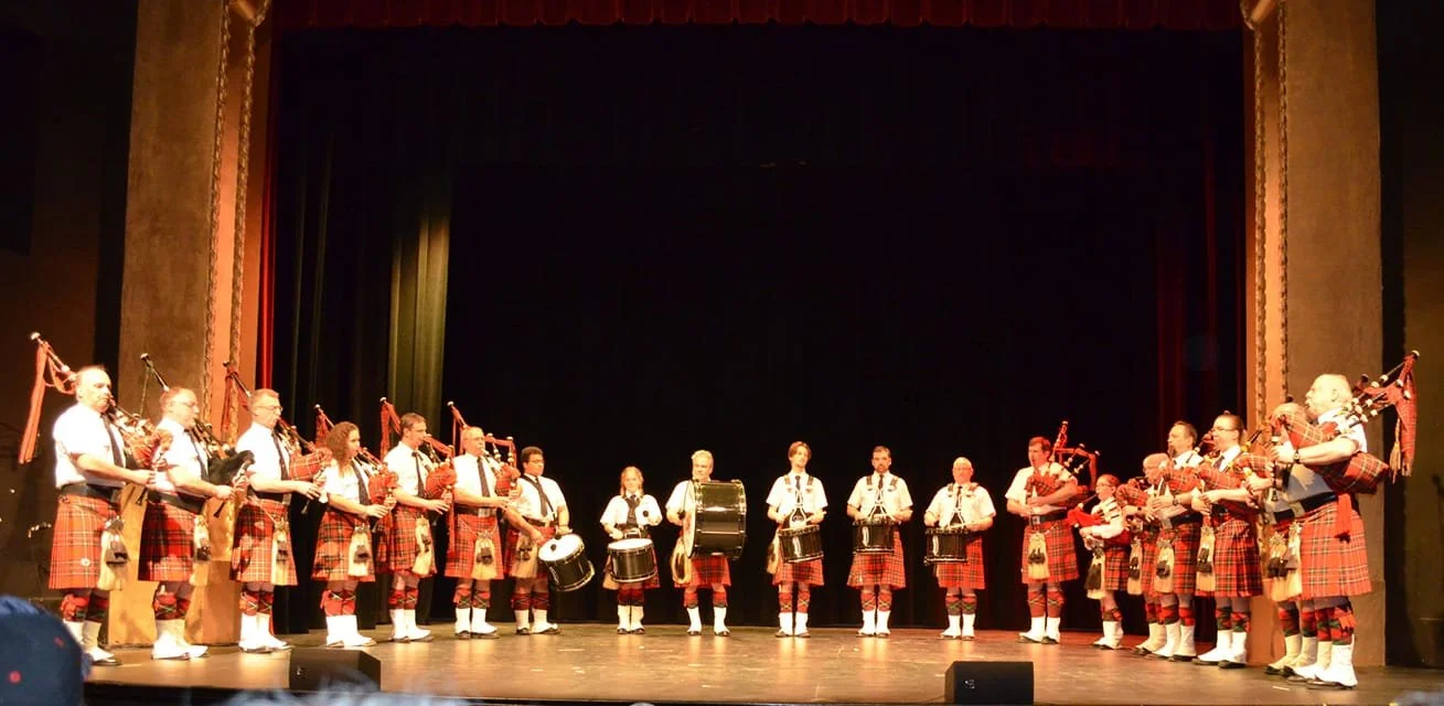 A group of musicians dressed in traditional Scottish kilts perform on stage with bagpipes and drums.