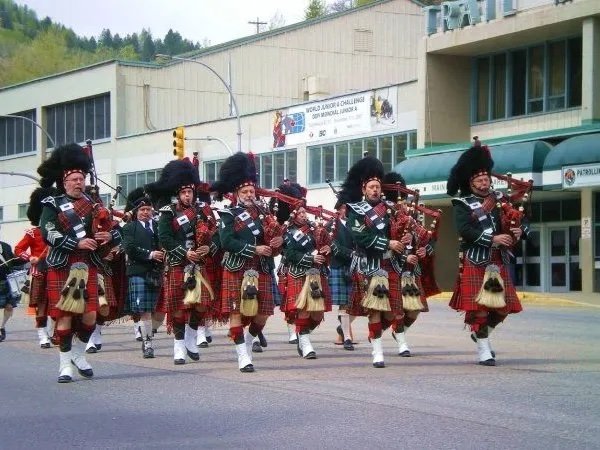 A marching band dressed in traditional Scottish attire, including kilts and hats with feathers, performing on a city street.