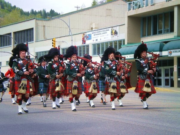 A group of people dressed in traditional Scottish Highland dress playing bagpipes as they march in a parade.