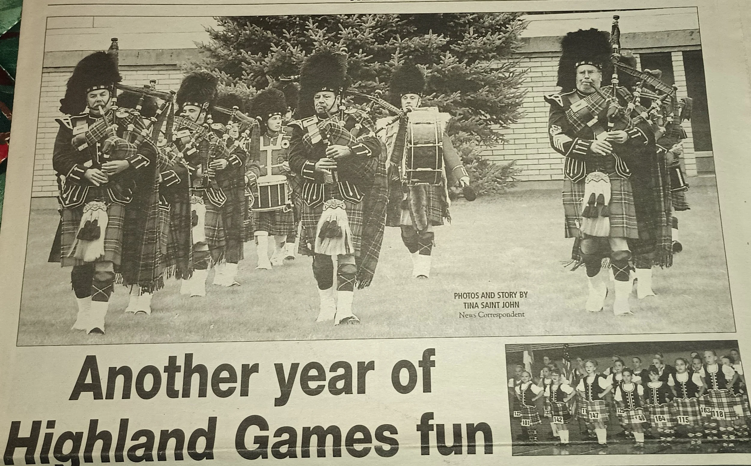 A black and white photograph of a parade with a group of bagpipers and drummers dressed in traditional Scottish kilts and jackets, marching outdoors in front of a tree and a building.