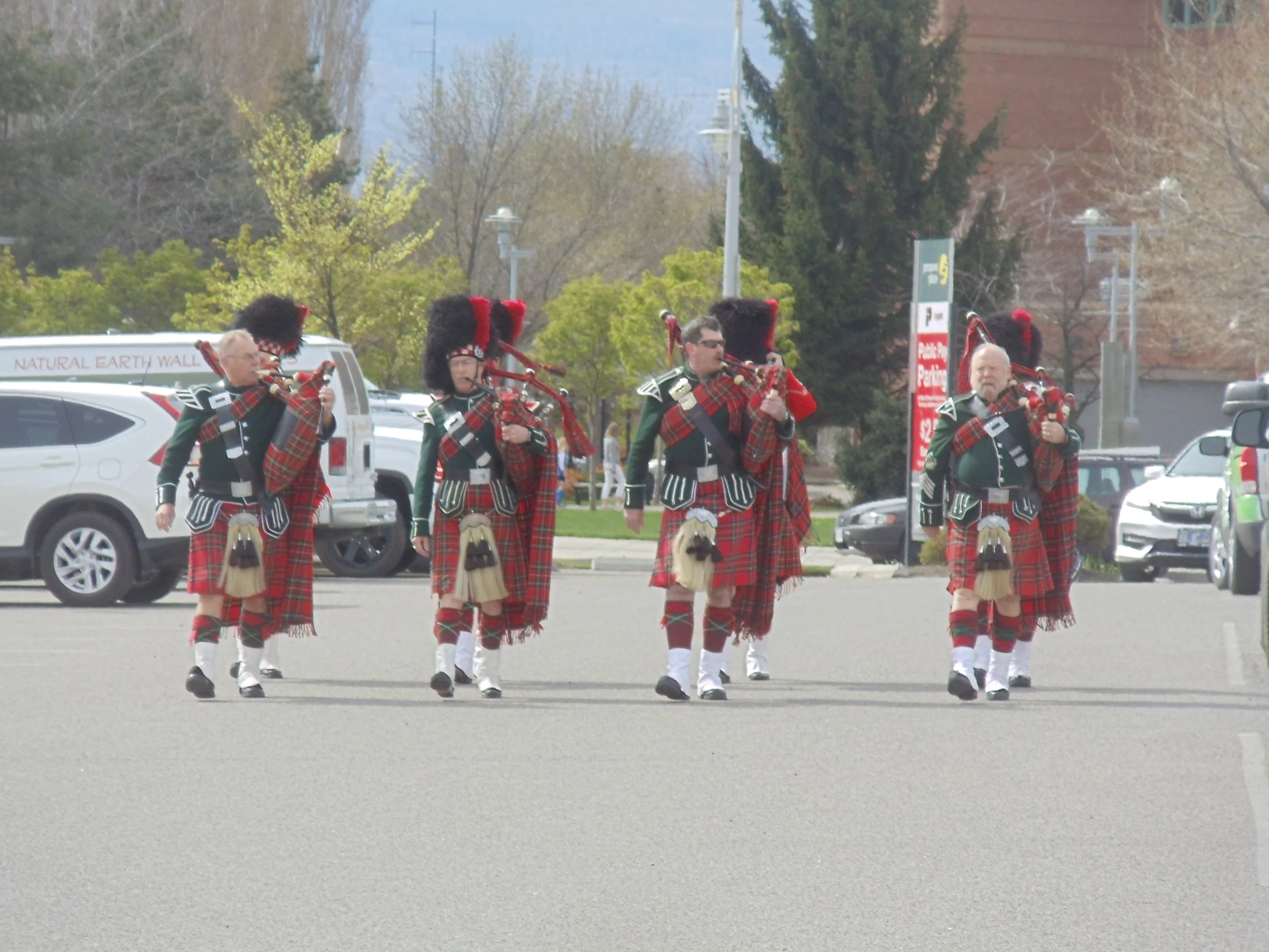 A group of five people dressed in traditional Scottish attire playing bagpipes in a parade on a city street.