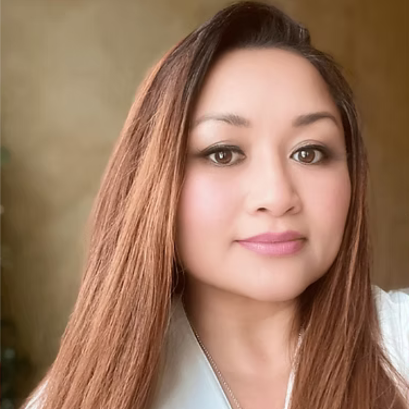 A portrait of a woman with long, reddish-brown hair, light makeup, and wearing a white top, in front of a neutral background.