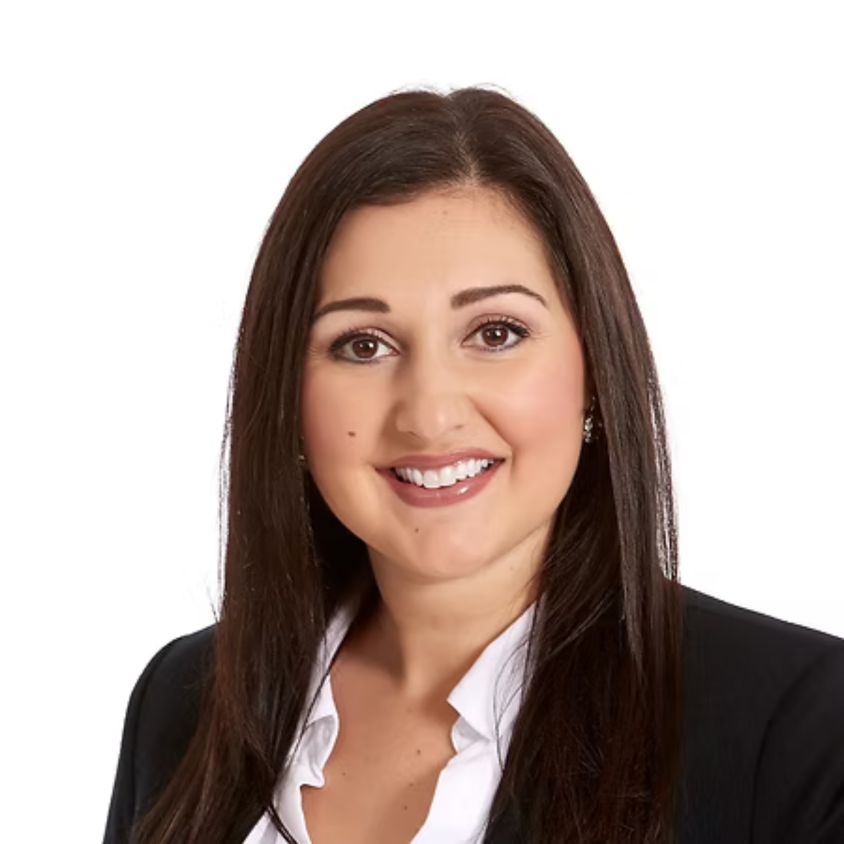 Professional headshot of a woman with long brown hair, wearing a black blazer and white shirt, smiling against a white background.