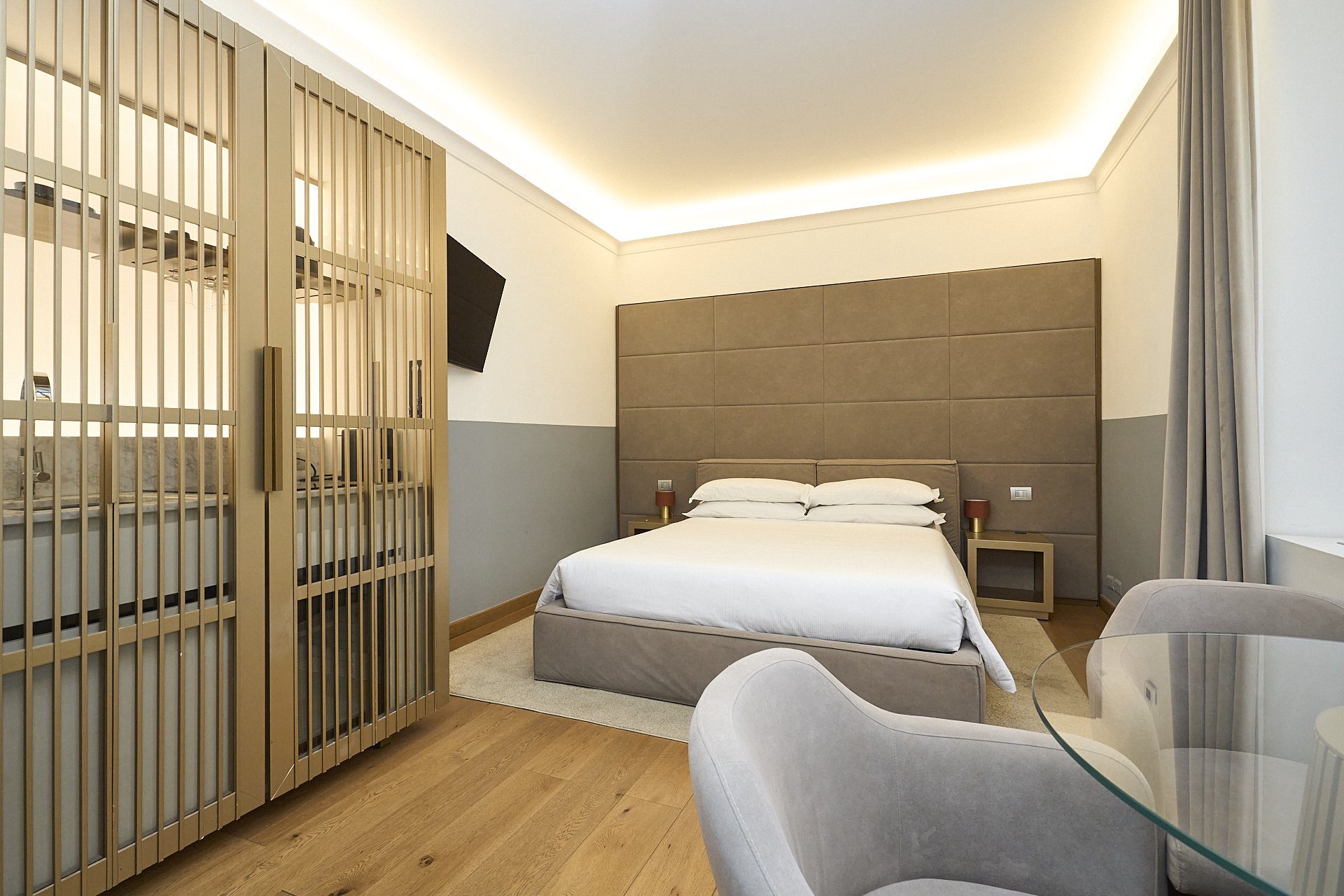 Camera da letto moderna con letto matrimoniale, testiera imbottita, due comodini con lampade, divisione con pannelli in tessuto e una finestra con tenda, pareti chiare e pavimento in parquet