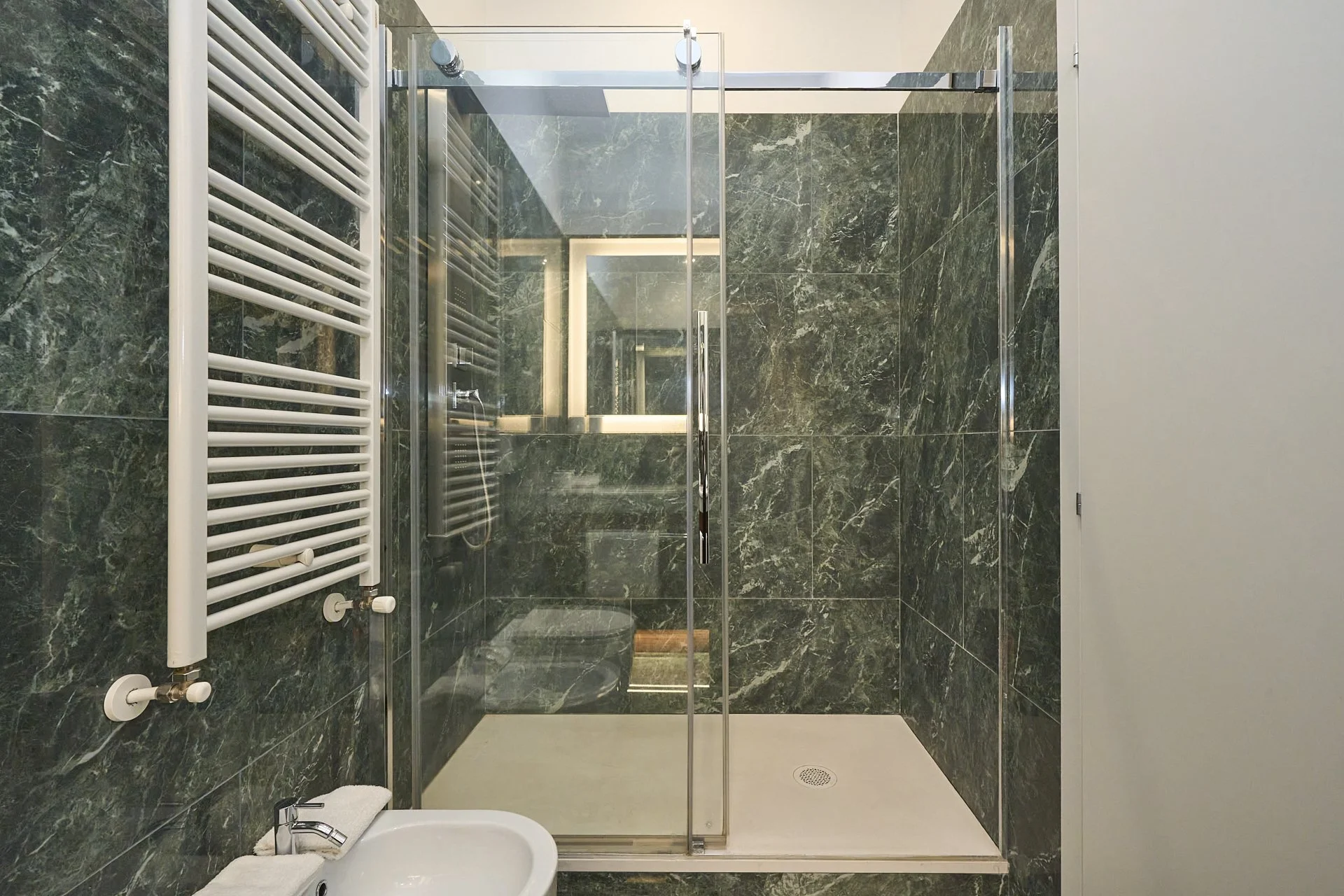 Stanza da bagno moderna con pareti di marmo verde, cabina doccia in vetro e asciugamano bianco.