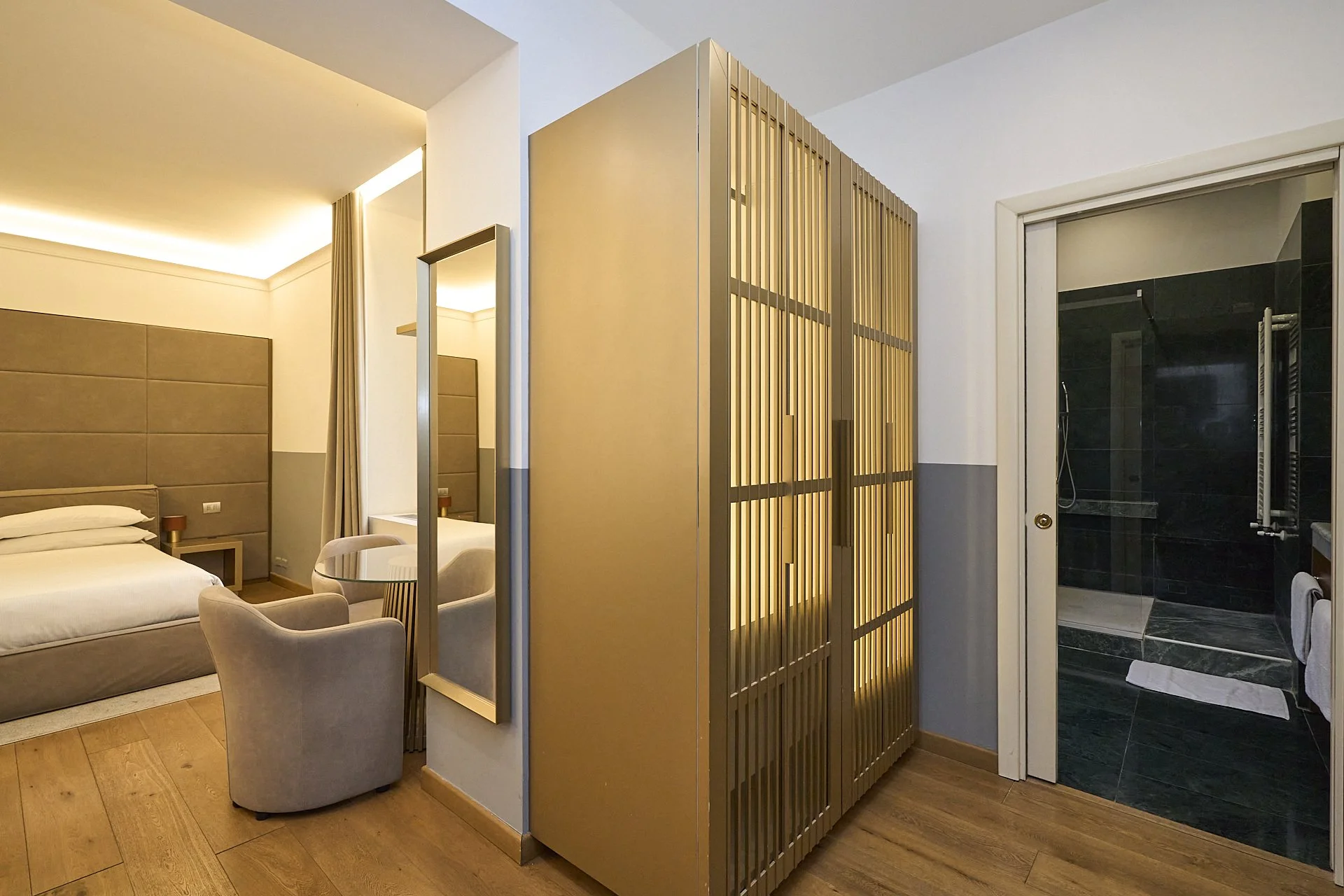 Camera d'hotel con letto, specchi, sedie e armadio, bagno con doccia.