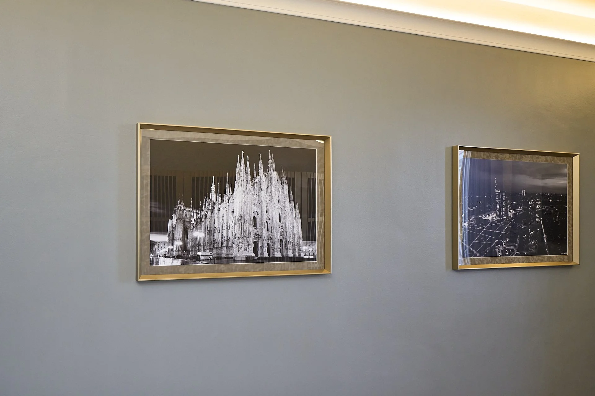 Due fotografie incorniciate appese a una parete, una raffigura il Duomo di Milano in bianco e nero e l'altra una vista notturna di una città con un grattacielo illuminato
