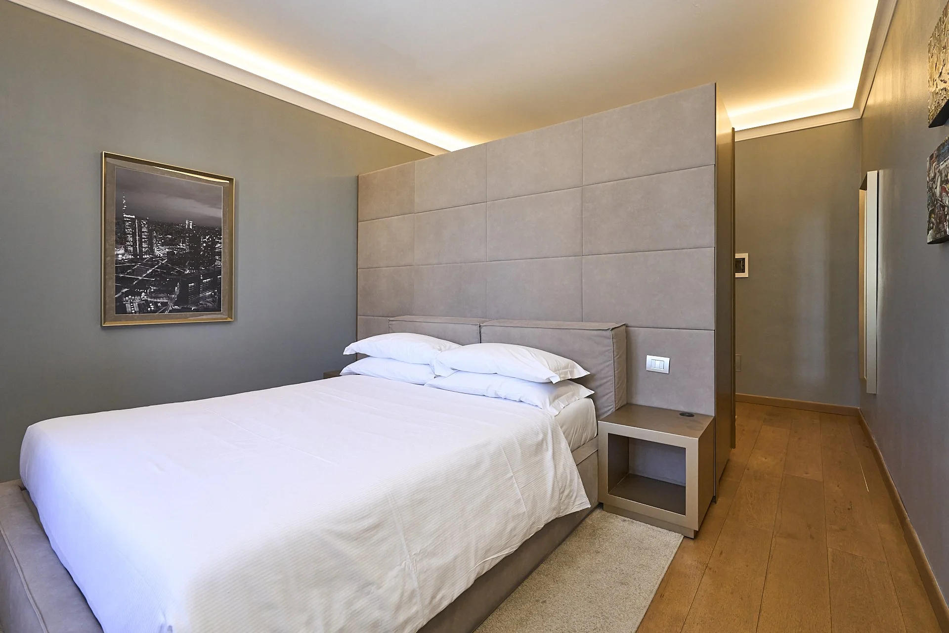 Camera da letto moderna con letto bianco, testata imbottita, pareti grigie, quadro in bianco e nero e pavimento in legno