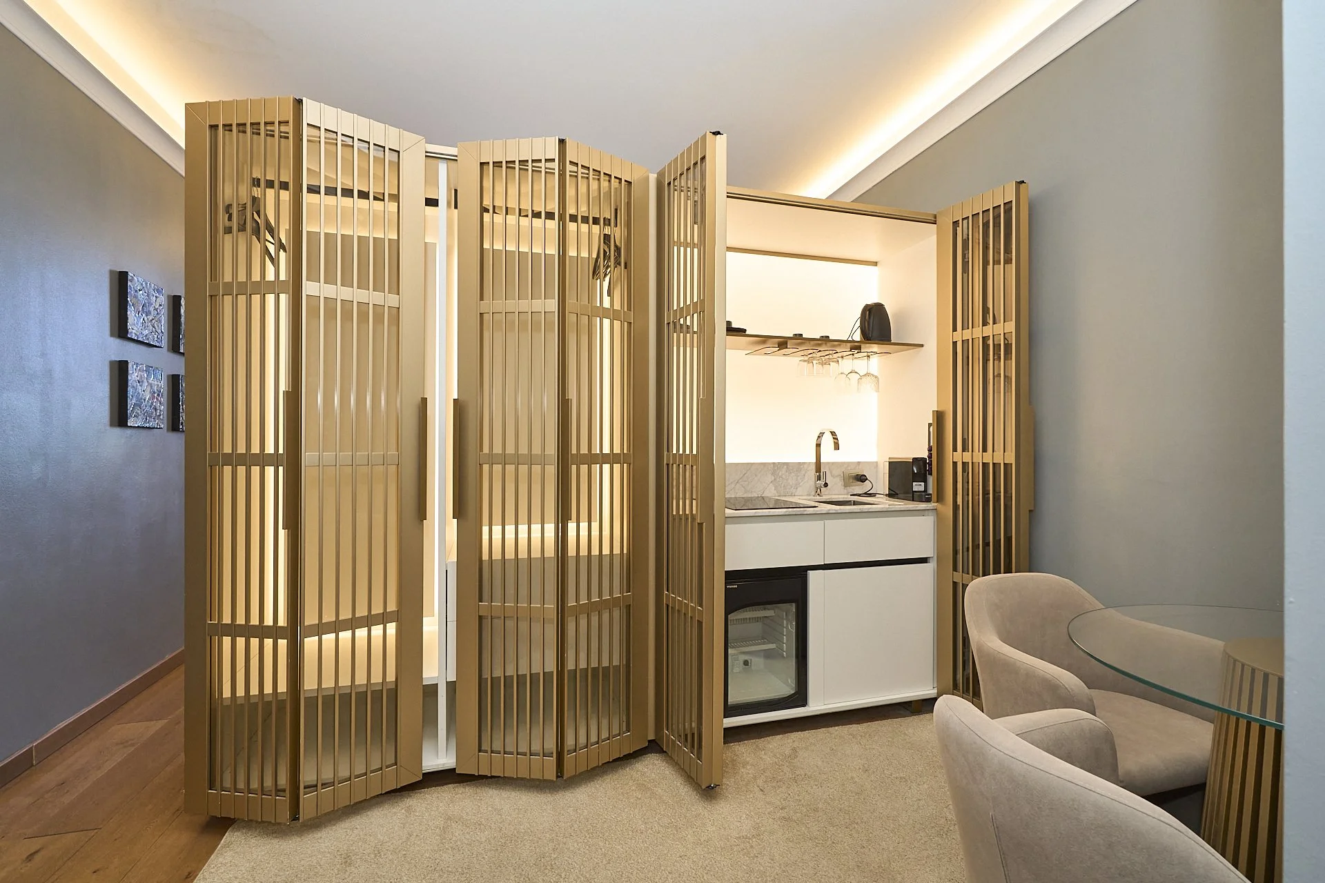 Angolo living con divani beige, zona bar con piccolo frigorifero, scaffale con bicchieri e macchina da caffè, bianca pareti e arredi in legno.