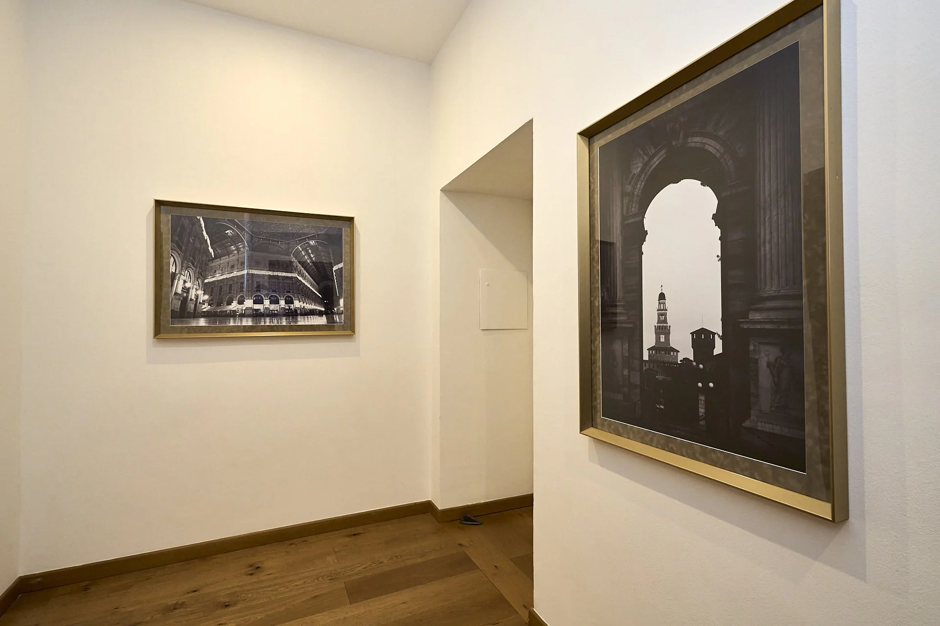 Due fotografie incorniciate appese a una parete in un museo, raffiguranti architetture storiche in bianco e nero.