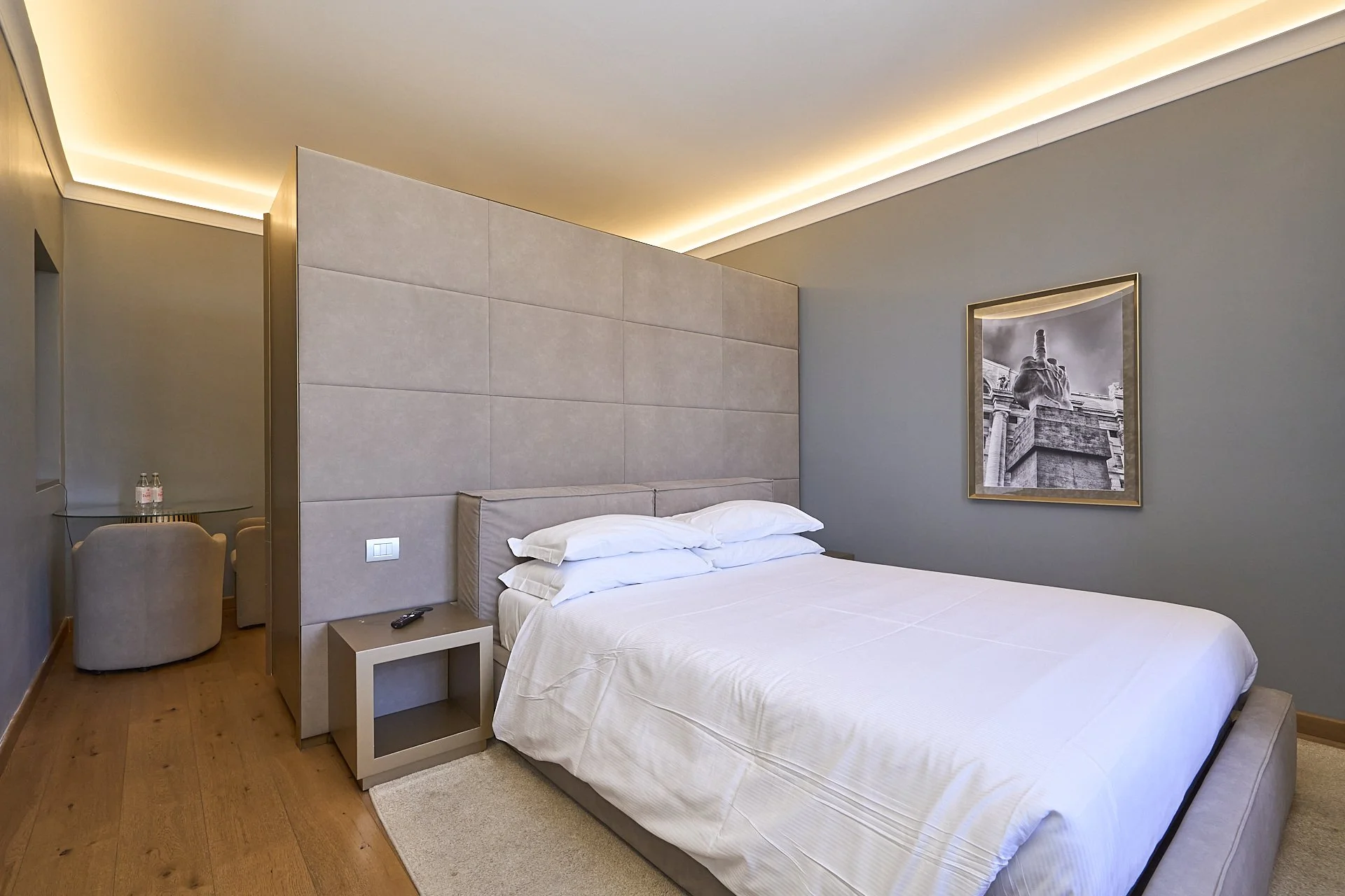 Camera matrimoniale moderna con letto grande, testata imbottita, pareti grigie e quadro in bianco e nero