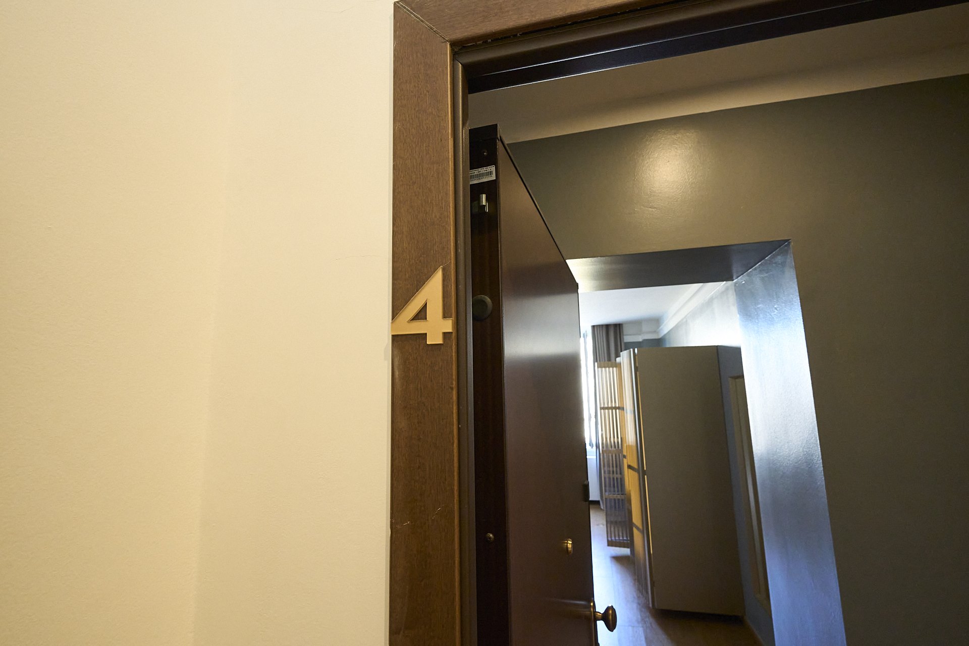 Poistello di un'aspirinetta in legno con un numero 4 in metallo in dotazione accanto alla porta di un appartamento o camera, con vista sull'interno di una stanza con mobili al suo interno.
