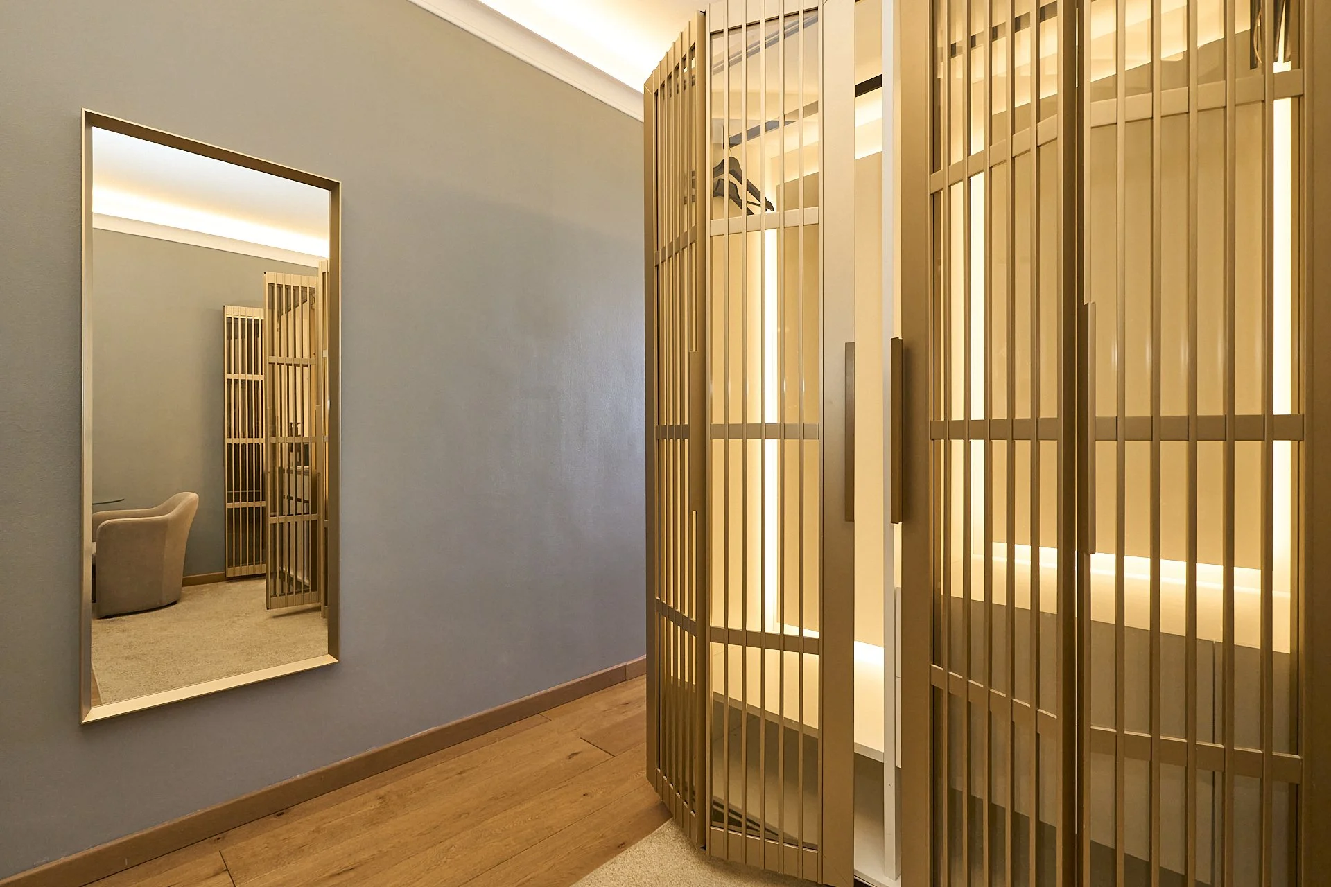 Interno di una stanza con pareti di colore blu e arredi in legno, con uno specchio sulla parete e una porta che conduce a un'altra stanza con una sedia imbottita.