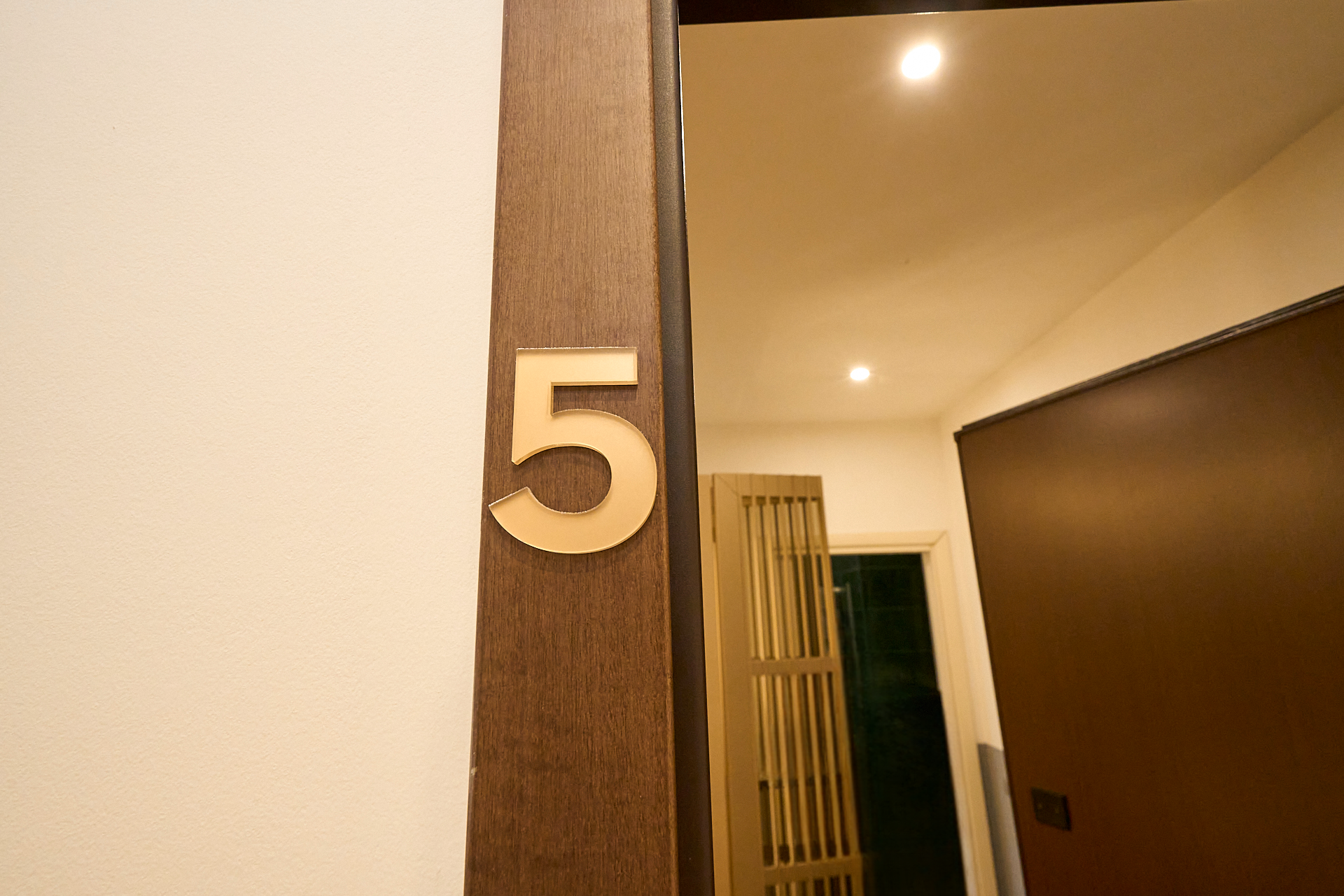 Particolare di una porta con il numero 5 in rilievo, in un interno con pareti chiare e un'illuminazione calda.
