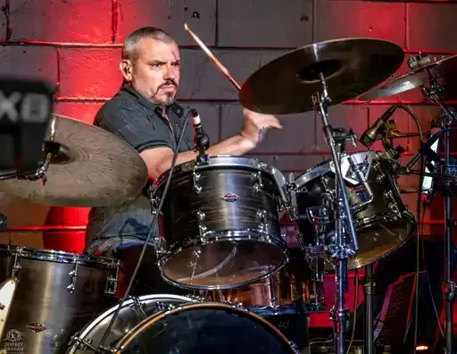 A man playing drums on stage with a red background.