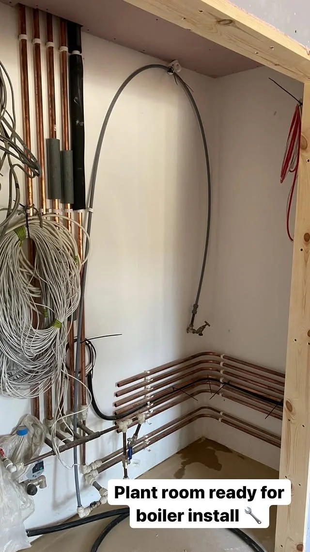 Plumbing and electrical lines installed in a room ready for boiler installation, with copper pipes on the wall and wires organized on the side.