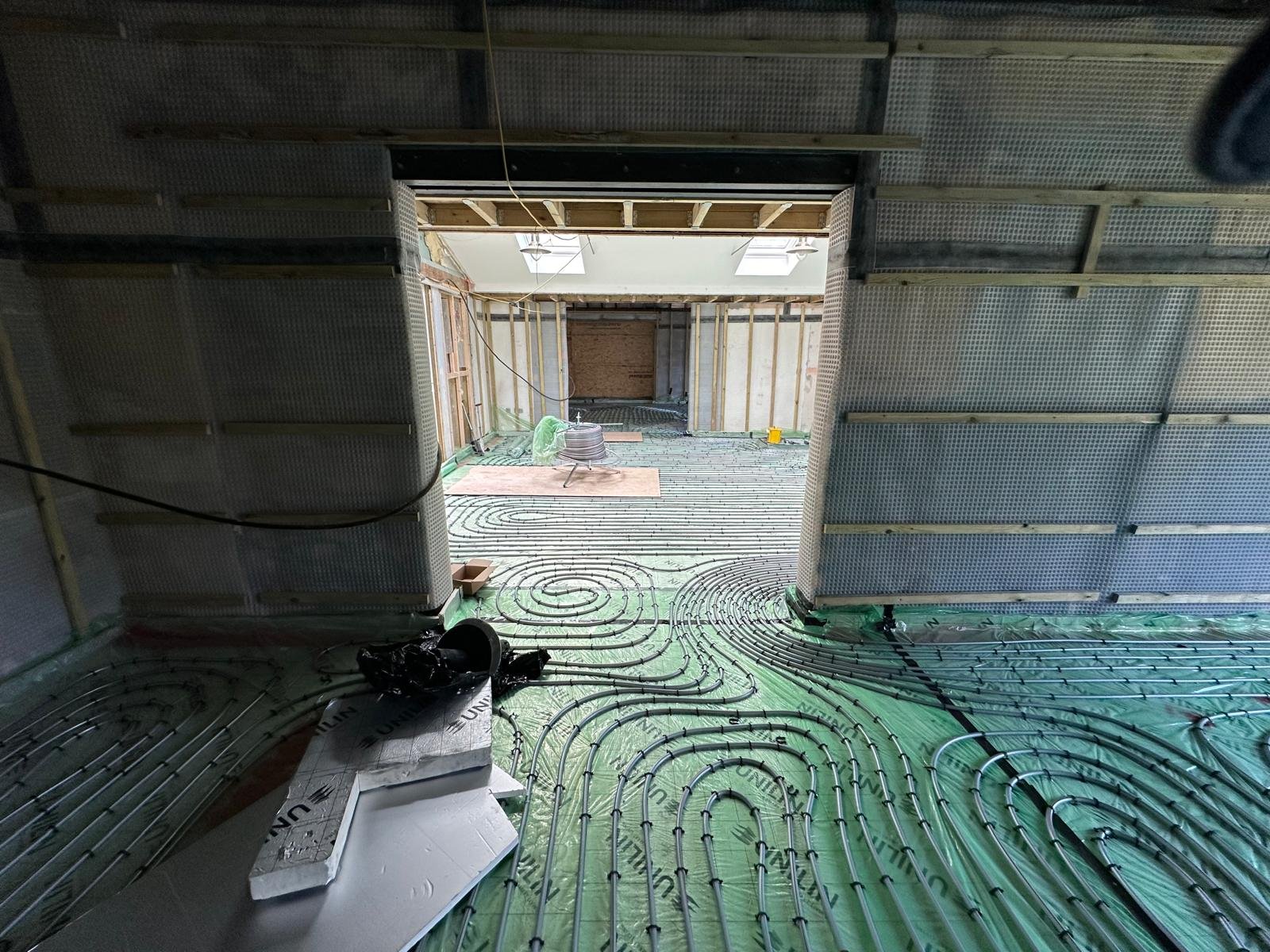 Construction site with underfloor radiant heating tubing installed, framing for walls in progress, and ceiling skylights.