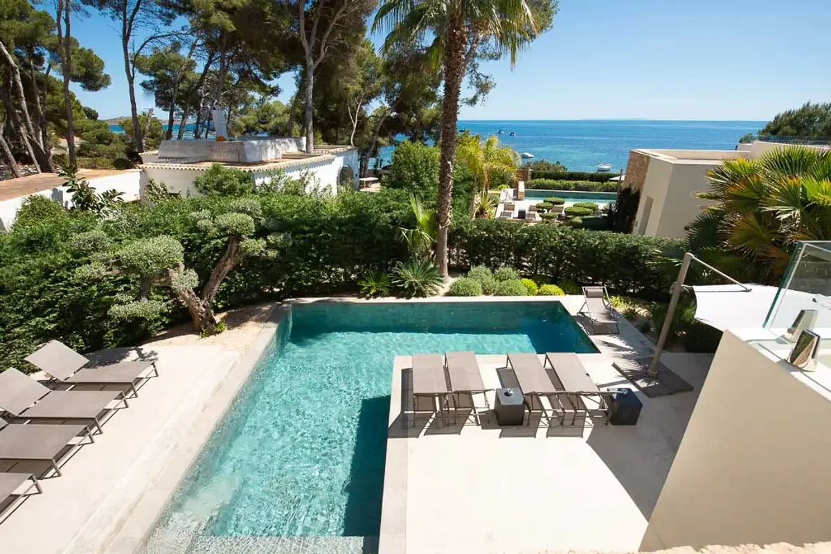 Luxury pool area overlooking the ocean with lounge chairs, surrounded by lush greenery and palm trees.