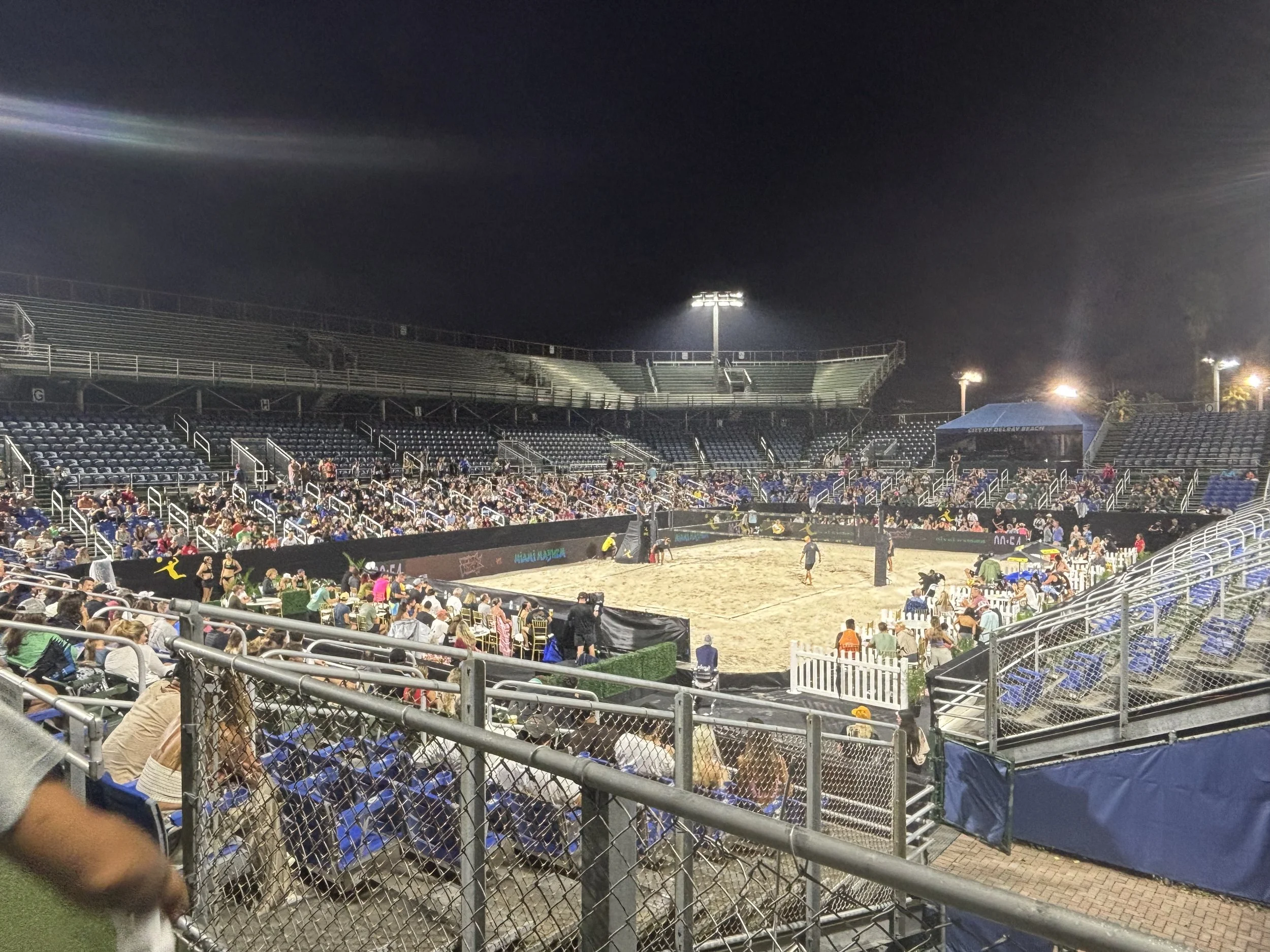 Spectators watching an outdoor AVP match under stadium lights