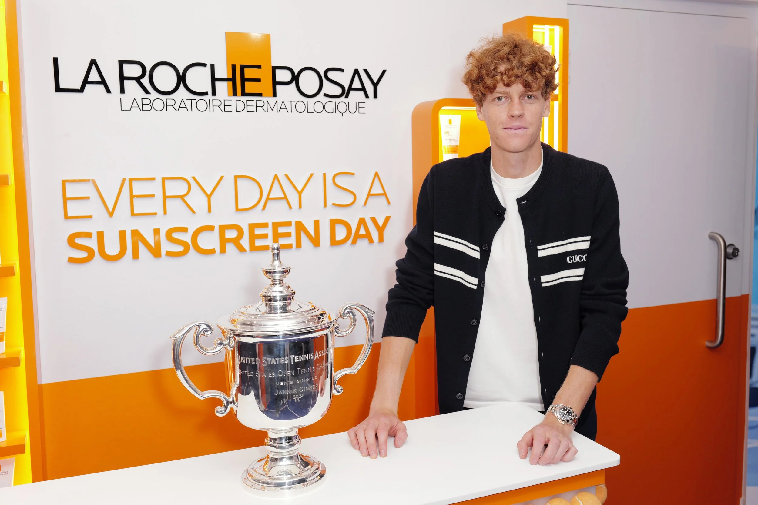 Tennis player posing with a trophy at the La Roche-Posay U.S. Open sunscreen display.