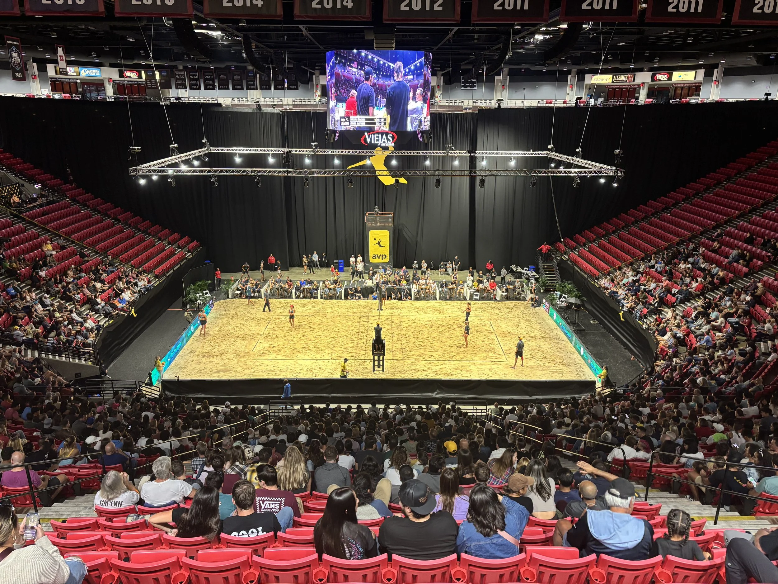 AVP sand court inside an arena with red spectator seating