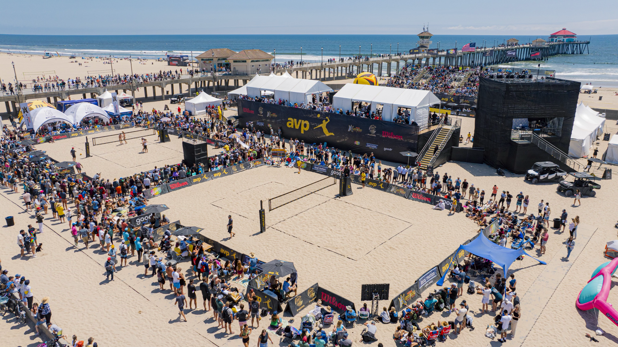 AVP beach volleyball courts, spectators, and hospitality tents beside the pier
