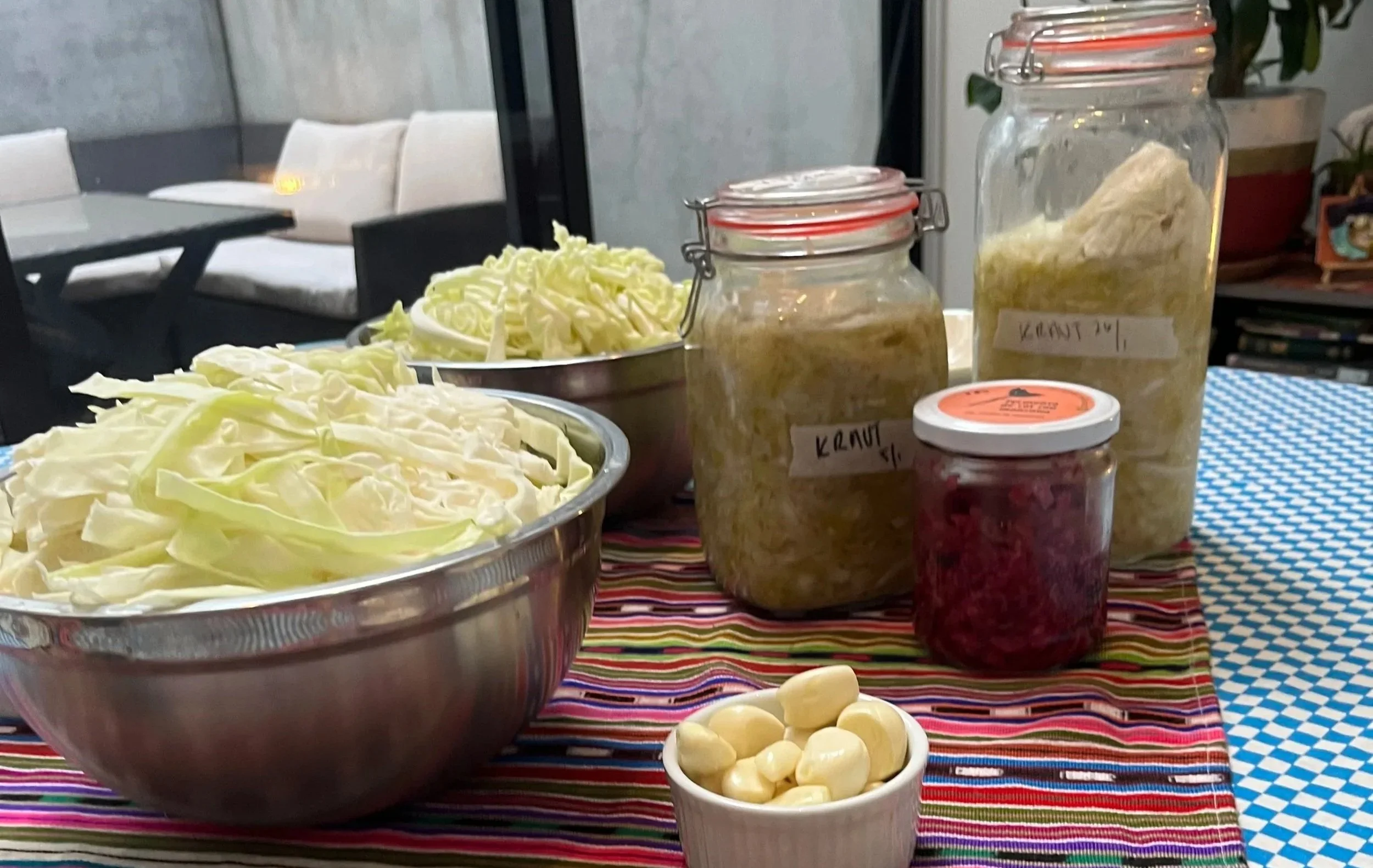 Assorted fermented vegetables and vegetables in jars on a colorful striped tablecloth.