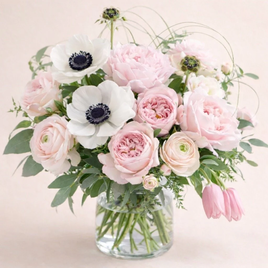 Romantic garden-style vase arrangement in soft blush and white. Features peonies, anemones, garden roses, ranunculus, tulips, and astilbe.