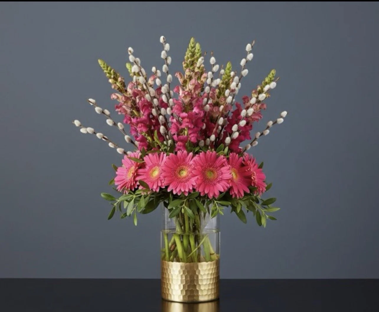 The Gerbera Edit features vibrant pink gerbera daisies arranged in a modern circular design with seasonal accents. Available for local delivery in Agawam, Feeding Hills, and nearby communities.