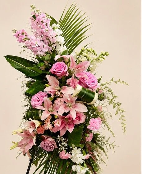 A bouquet of pink roses, lilies, orchids, and other flowers with green leaves and foliage.