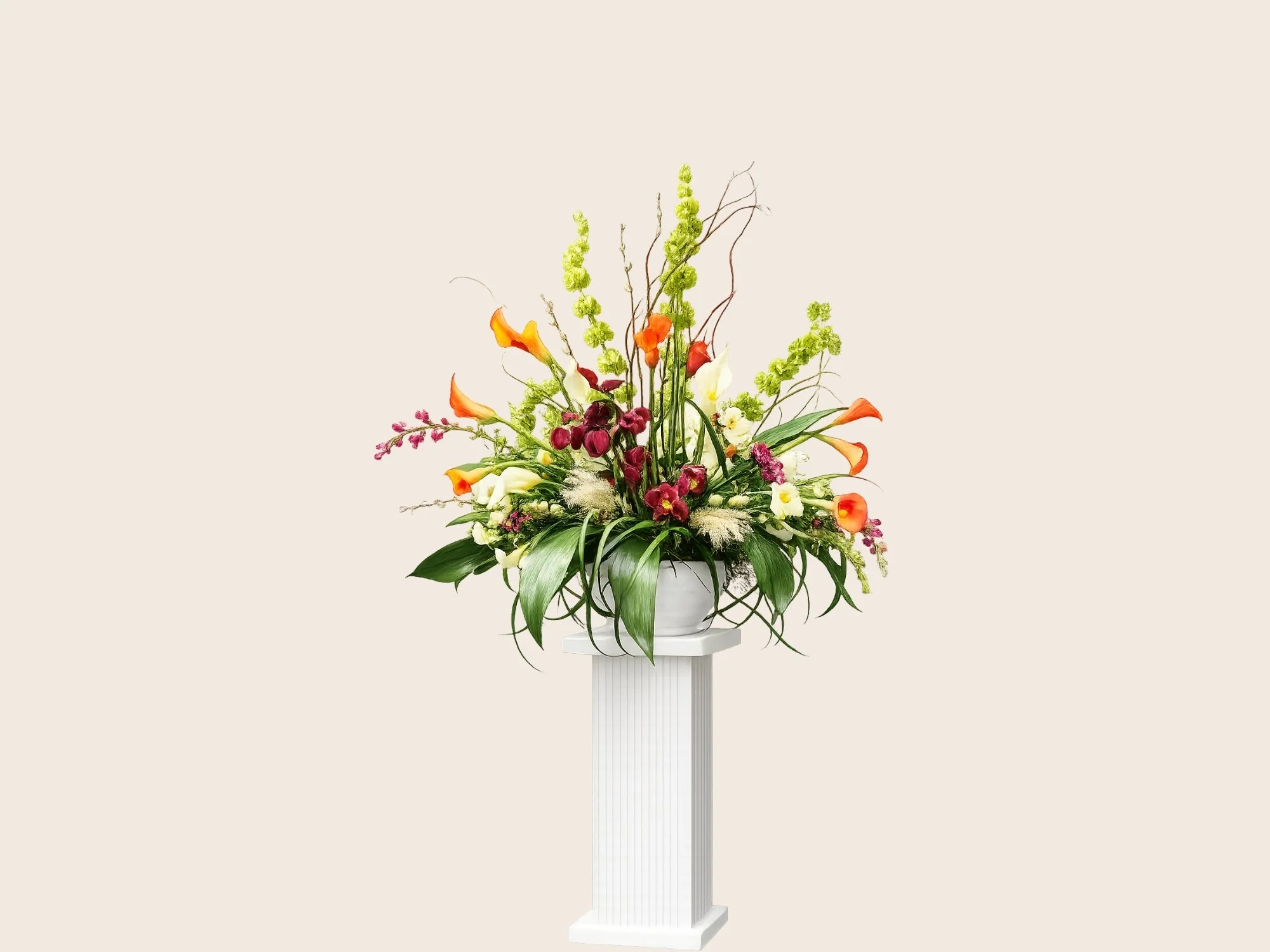 A large floral arrangement with white, orange, yellow, and purple flowers on a white pedestal against a plain light beige background.